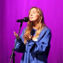 Singer at a microphone in front of a purple background.