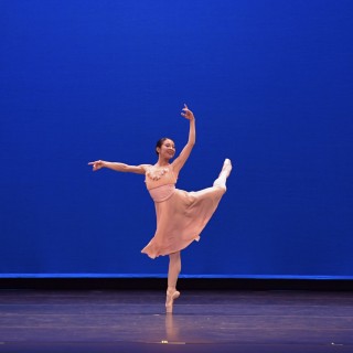 A female ballet dancer in a pink dress on a stage doing a pirouette
