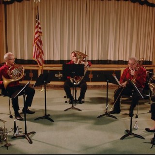 a group of Garden State Philharmonic musicians in red shirts and black pants performing in a theatre with a white curtain