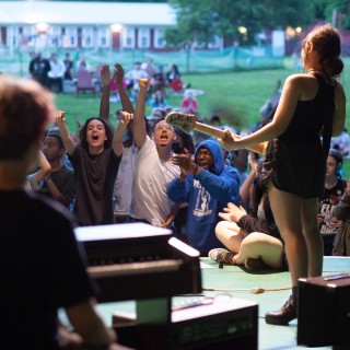 girl plays guitar on outdoor stage for excited crowd