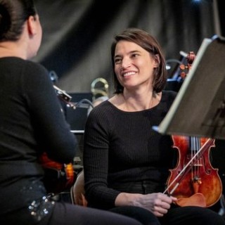 two female musicians holding violins take a break to talk between songs