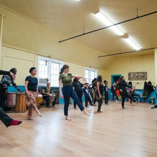 a dance rehearsal in a yellow and blue practice room, dancers pointing their fingers and toes
