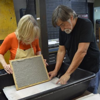 Two older people using a mould and decker to make paper