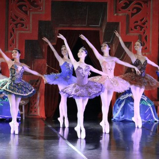 Young women in different color tutus and white tights perform en pointe ballet on stage