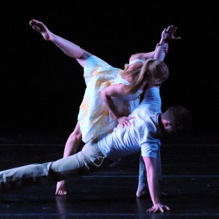 A pair performing a dance duet on a dark stage