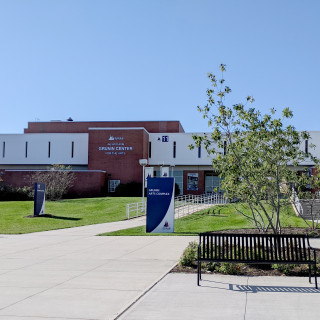 Building complex with red brick and white facade, labeled "Grunin Center for the Arts," surrounded by greenery and benches u