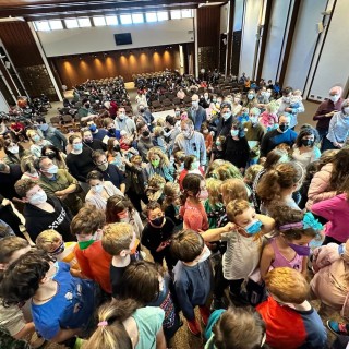 a large crowd of mostly children in COVID-19 masks packed into an auditorium