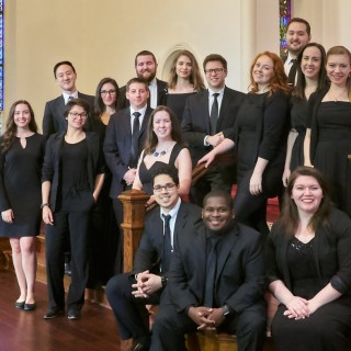 The Glassbrook Vocal Ensemble in all black outfits smiling for a photo in a church