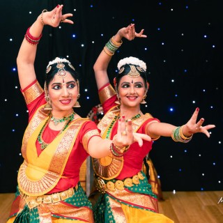 Two women posing in red, green, and gold traditional Indian dance costumes