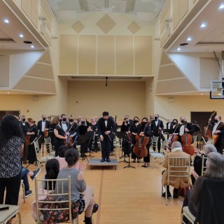 a conductor bows in front of his ensemble while people in yellow chairs clap for him