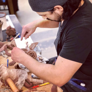 a man in a black shirt works on a piece of brown clay that has been shaped into a rose