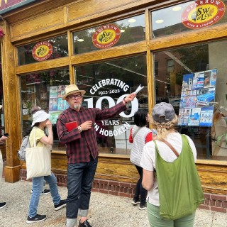 A group of people standing in front of a store pointing at a sign that says “Celebrating 100 Years in Hoboken”