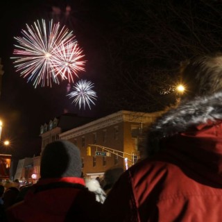 A group of people in coats standing in town watching fireworks