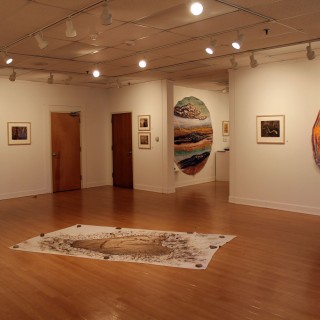 An empty art gallery with three textured circular paintings on the walls