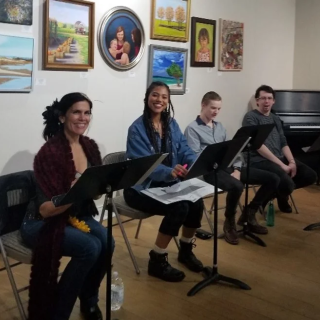 four players sit in front of music stands in a practice room