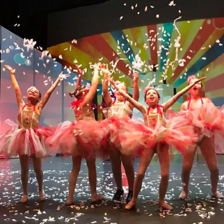 a troupe of ballerinas in pink tutus dance under a cloud of confetti