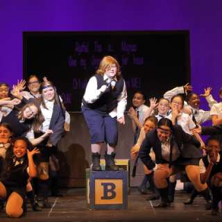 children performing a production of the musical Matilda, wearing school uniform costumes and singing