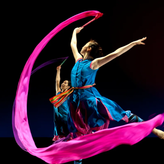 Two dancers are performing with a pink and blue ribbon