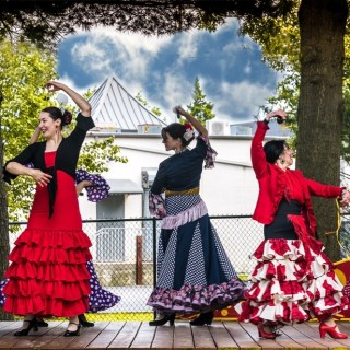 A group of people in Flamenco dresses dancing on a wooden deck.