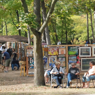 wooden art display grids of paintings set up in the woods for people to browse and shop