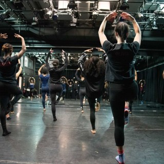 people in all black rehearsing a dance in front of a mirrored wall