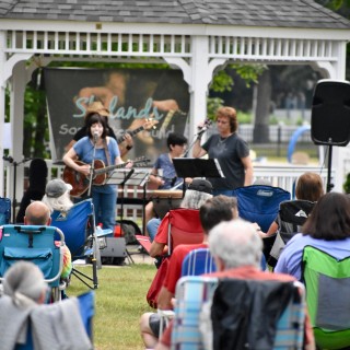 A group of people sitting in lawn chairs watching a band perform in front of a gazebo.