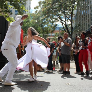 A man and woman wearing white dancing on a street for spectators