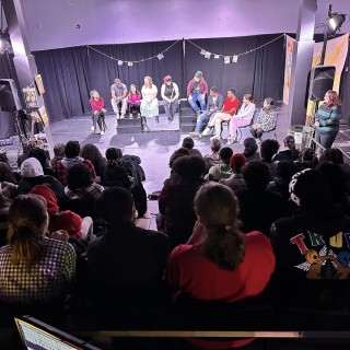 A group of actors on stage speaking to audience memebrs