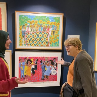 Two women standing in front of a display of art smiling and discussing the artwork.