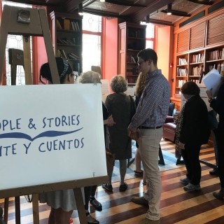 A group of people standing in a room full of bookshelves and a sign that says, “People & Stories Gente Y Cuentos.”