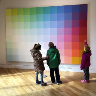 Three people stand in front of a color gradient mosaic art piece at the Visual Arts Center of New Jersey.