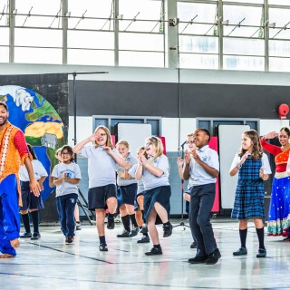 A group of children in a bright auditorium learning Bollywood dancing from Amit Shah.
