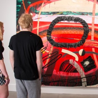 Two people viewing art on the wall.