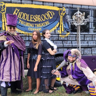A group of actors posing in front of a Riddlesbrood Touring Theatre Company tour bus