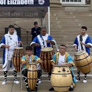 Five men playing drums at the base of stairs leading up to a building.