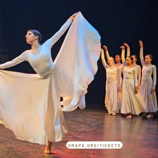 A group of dancers in white dresses on stage