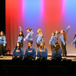 Children on a stage with a blue and red background pose in triumph.