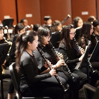 Children in an orchestra, wearing all black, playing their instruments.