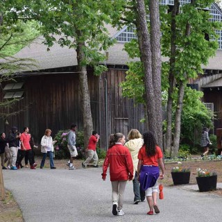 People walking in a wooded area amongst wooden sided buildings at WheatonArts.