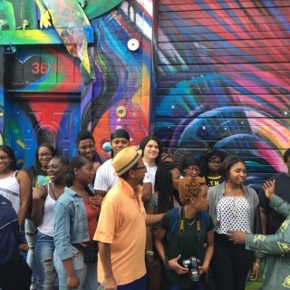A group of young people and teachers in front of a mural.