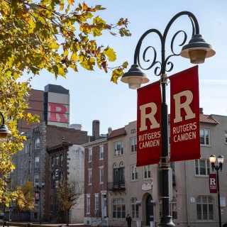 Rutgers Camden banners on a light pole, displayed on a bustling city street with urban buildings in the background.