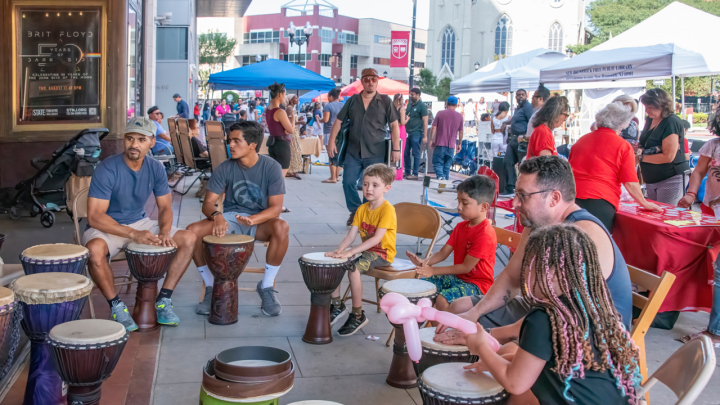 Children and adults sitting in a circle on the sidewalk playing drums
