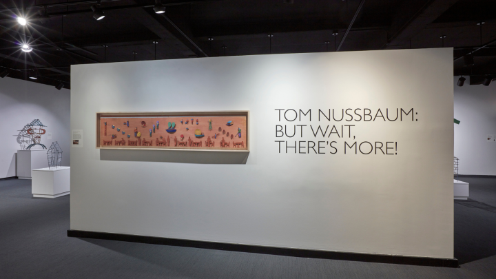 Gallery wall that reads "Tom Nussbaum: But Wait, There's More!" with a work of art to the left
