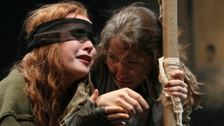 Actor blindfolded next to another actor holding onto a pole