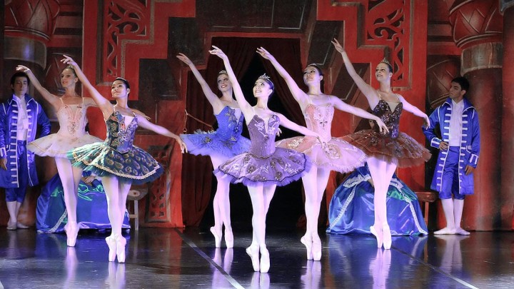 Young women in different color tutus and white tights perform en pointe ballet on stage