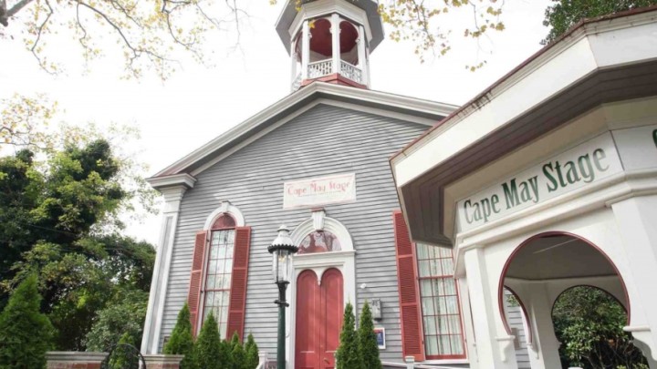A brightly colored gothic building with a gazebo in front with the sign “Cape May Stage” sign on it