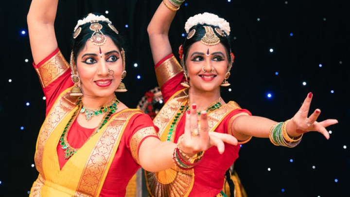 Two women posing in red, green, and gold traditional Indian dance costumes