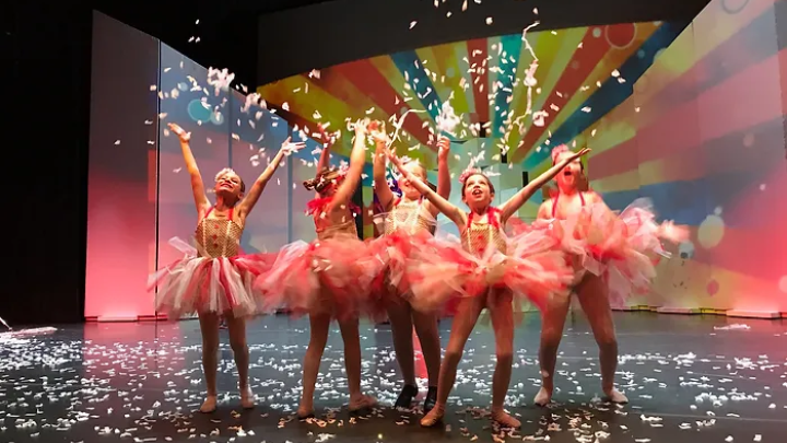 a troupe of ballerinas in pink tutus dance under a cloud of confetti