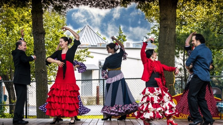 A group of people in Flamenco dresses dancing on a wooden deck.