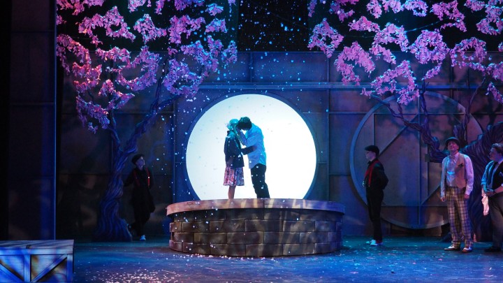 The Fantasticks, A moon and flowering trees with a couple kissing.